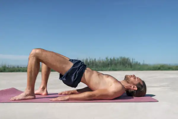 Homme en posture de pont sur un tapis, explorant comment trouver le périnée chez l'homme.