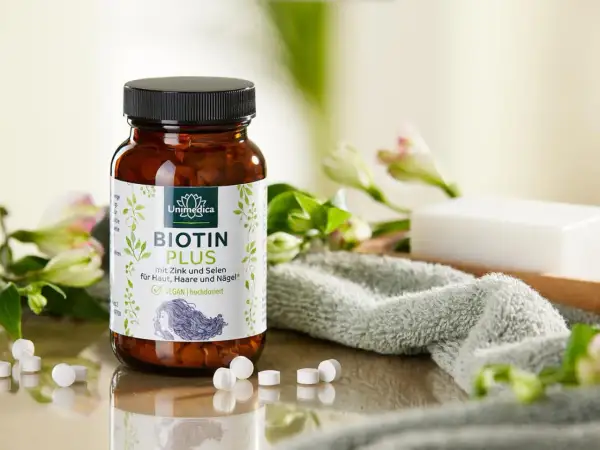 Flacon de Biotin Plus, une réponse à quelle vitamine pour les ongles, avec des fleurs et une serviette.