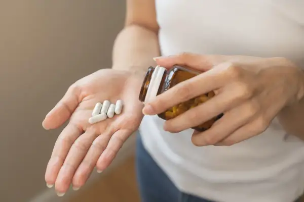 Main tenant une pilule dans sa paume, une personne verse des capsules d'un flacon. Une cure de vitamine D pour le bien-être.