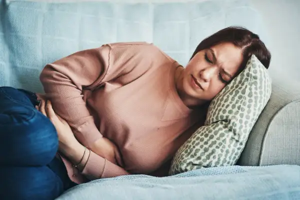 Femme souffrant de SPM, se tenant le ventre sur un canapé. Combien de temps avant que la douleur ne passe ?