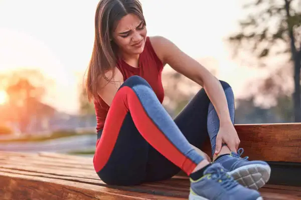 Une coureuse s'assoit sur un banc, se tenant la cheville avec une expression de douleur. La douleur à la cheville après la course à pied peut être débilitante.